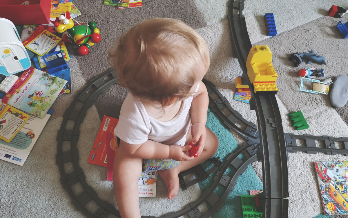 Kind sitzt im Kinderzimmer zwischen Spielzeug und Eisenbahn