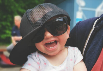 Lachendes Kind mit Sonnenbrille und Baseball-Cap